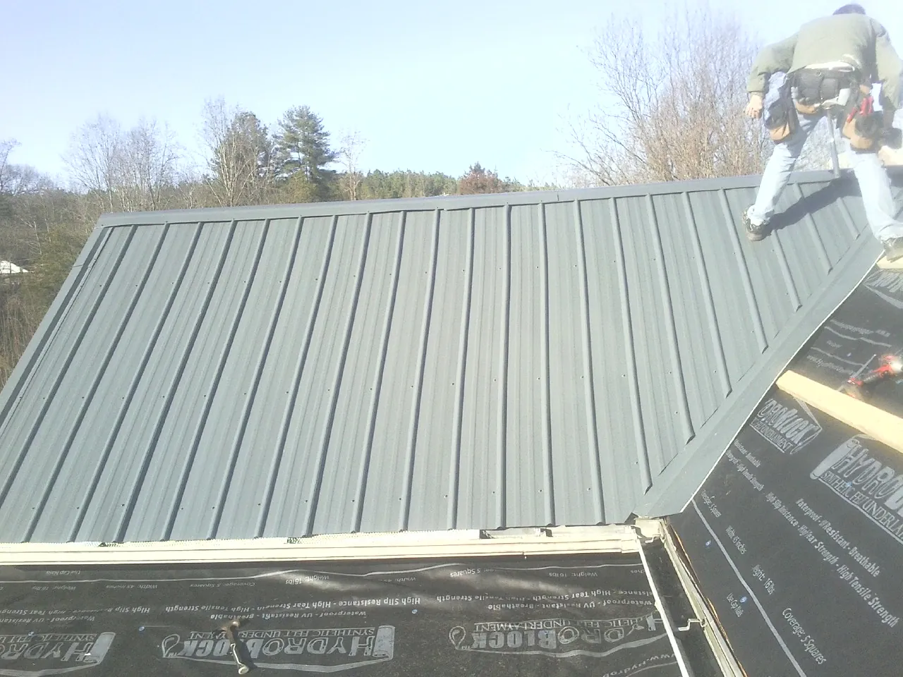 Crew installing dark green standing seam panels over synthetic underlayment in Swiftwater