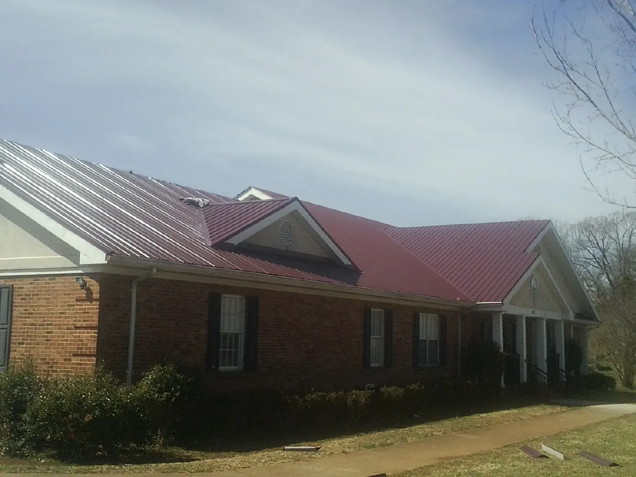 Red metal roof with gabled entries on a long brick building, from a Hail Damage Roof Repair job in Swiftwater