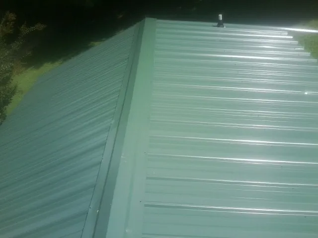 New green metal panels meeting at the ridge of a roof — Flat Roof Repair work by our crew in Swiftwater