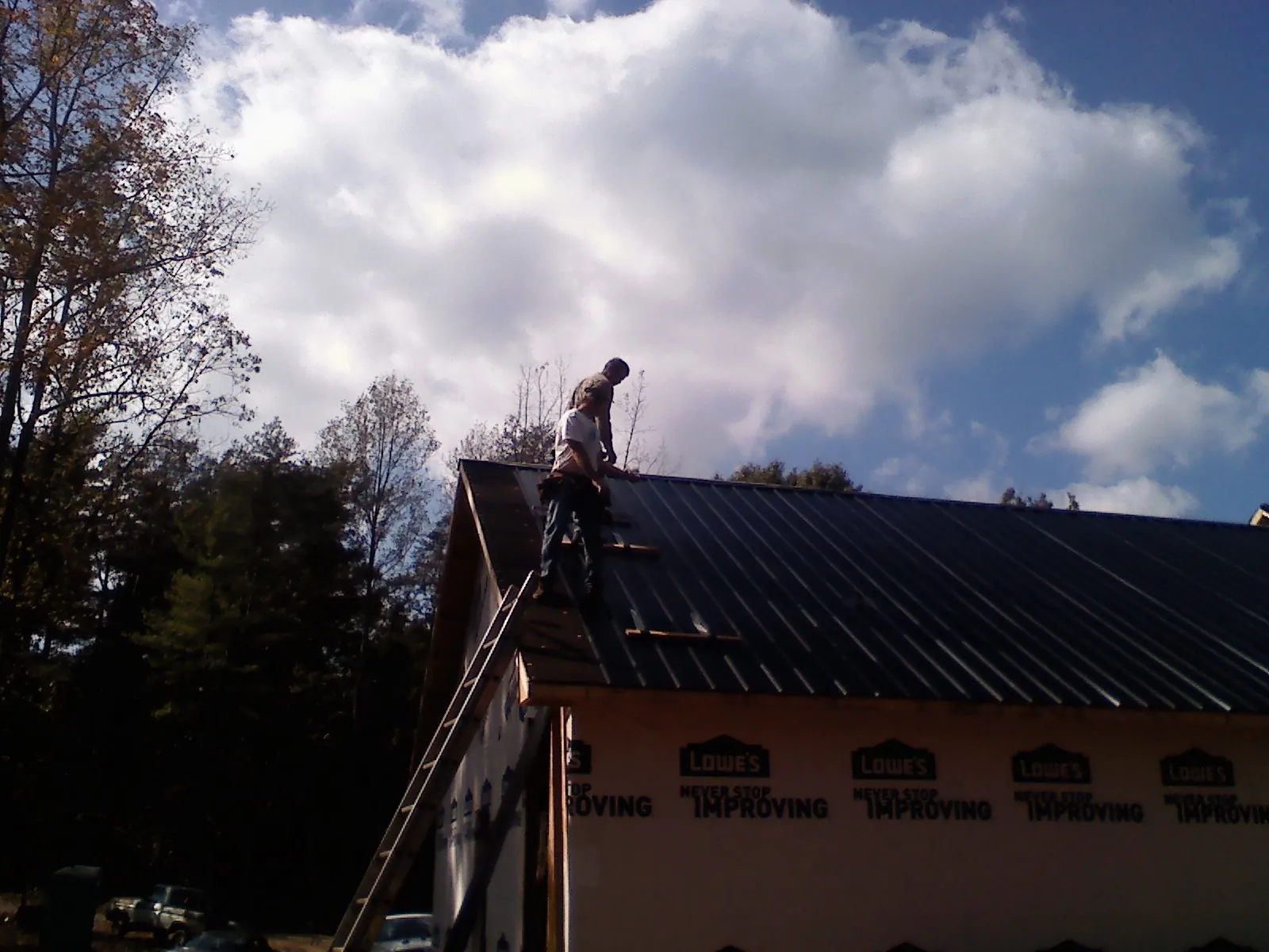 Roofer fastening dark metal panels high against a cloudy sky, from a Roof Inspection job in Swiftwater