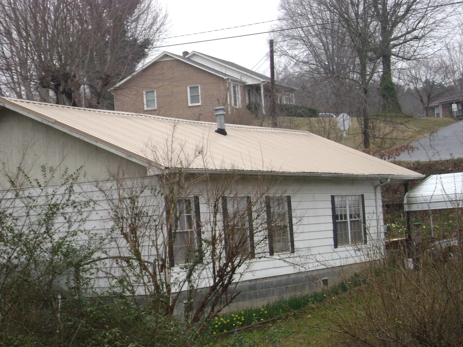 Tan metal roof on a white sided house set into a hillside — Commercial Roofing by Roofing Brothers in Swiftwater