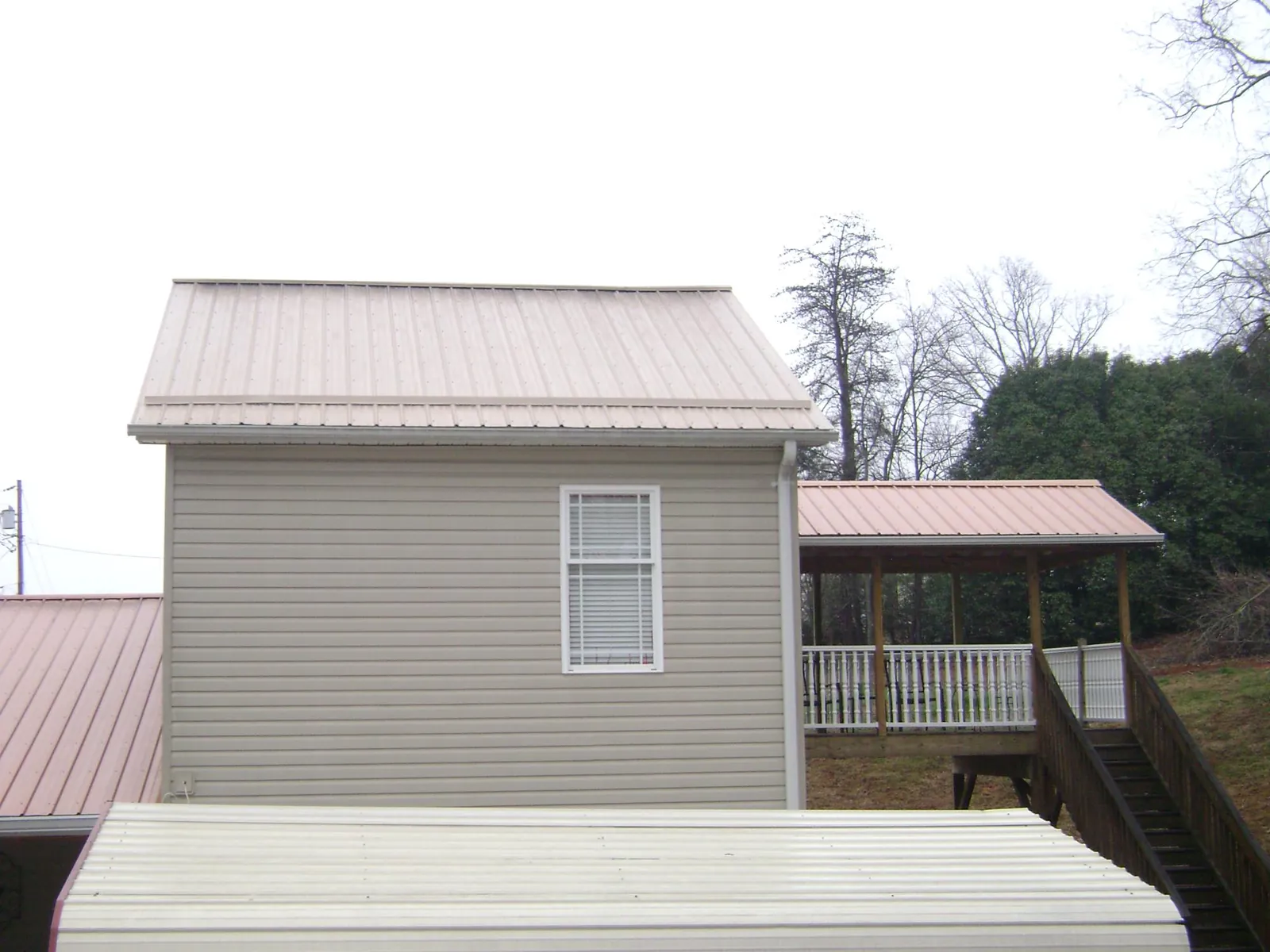 Tan metal roofs on a two story addition and attached porch, from a Roof Replacement job in Swiftwater