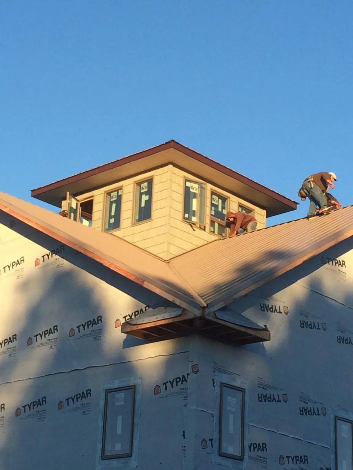 Roofers working around a rooftop cupola on a new metal roof at sunset — Roof Waterproofing in Swiftwater by Roofing Brothers
